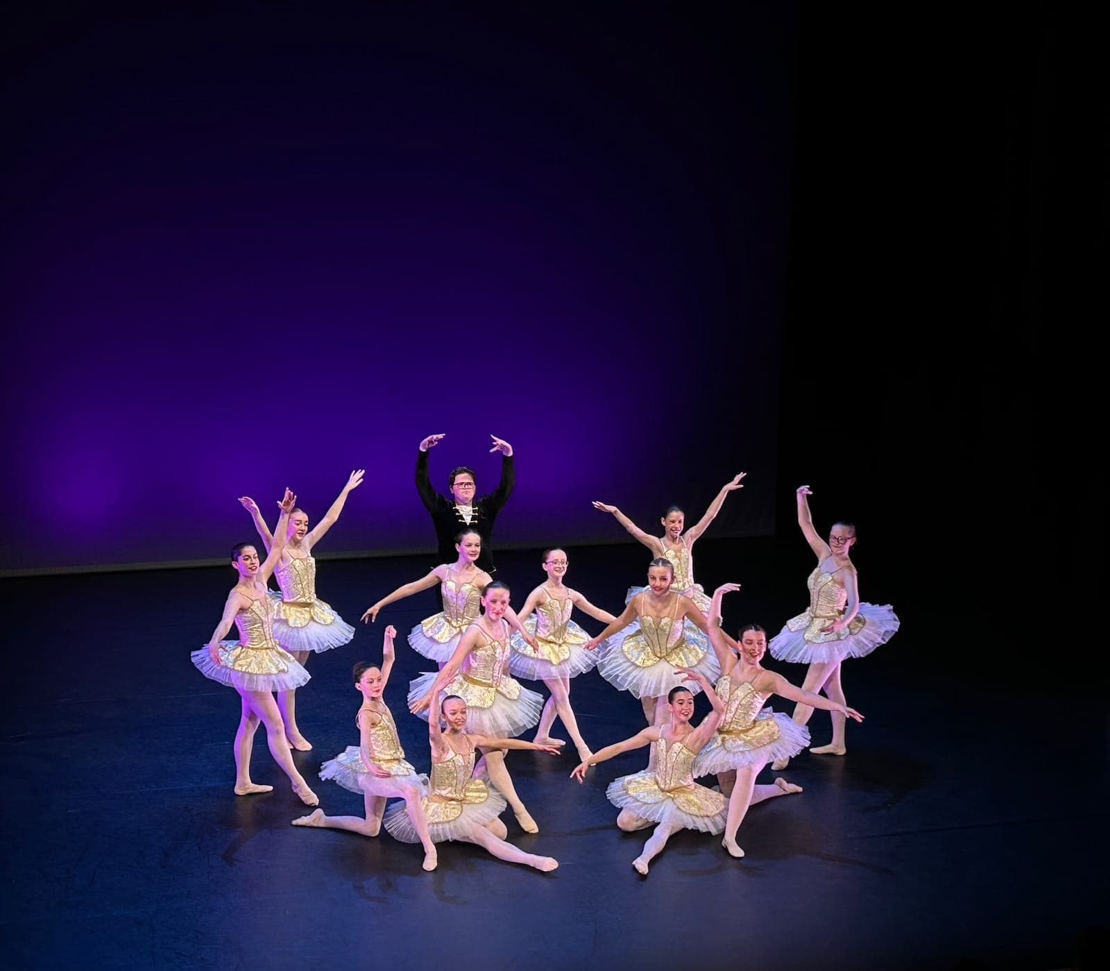 A ballet ensemble in white tutus posing on a dark stage