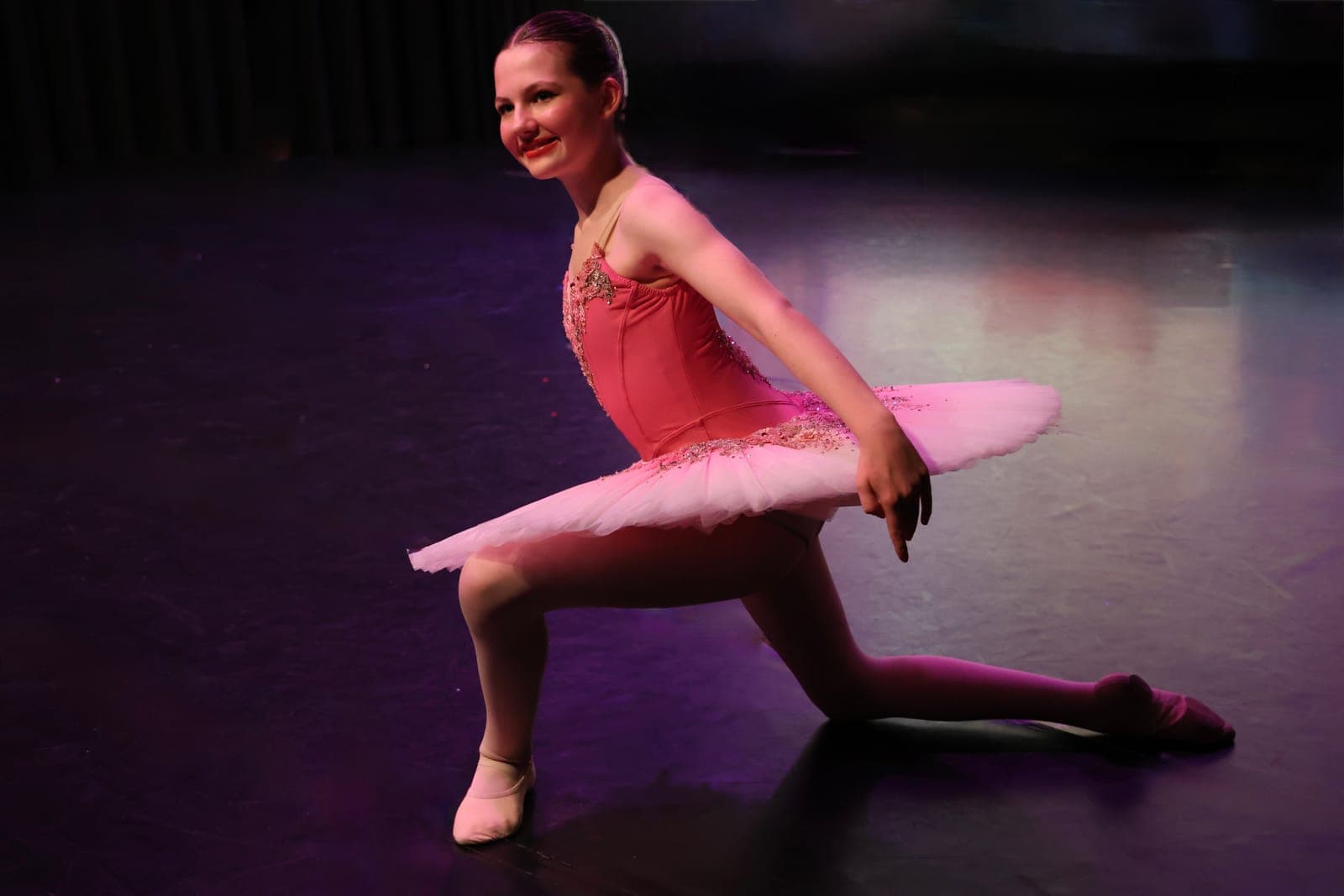 Young ballerina in a pink tutu kneeling on stage