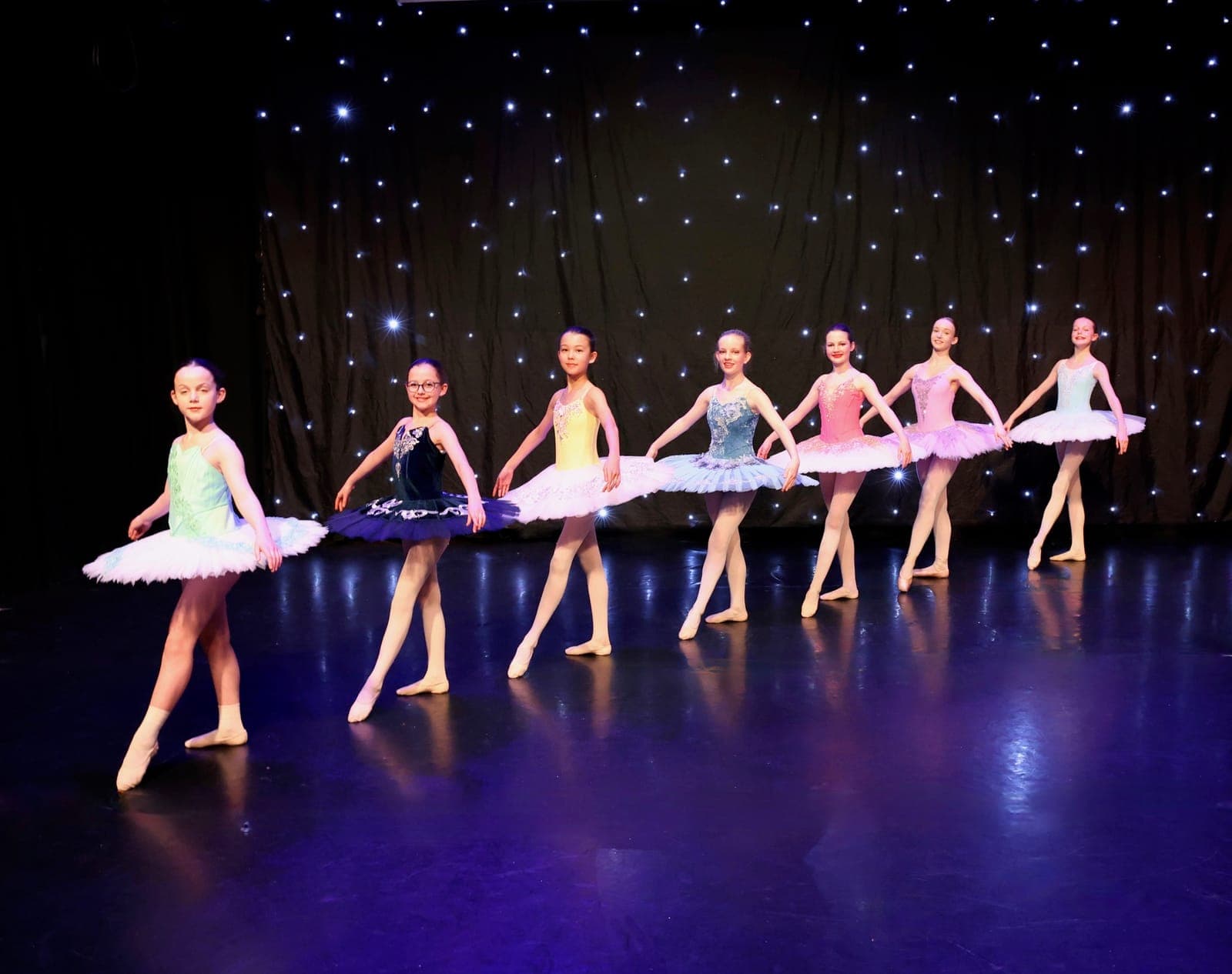 A line of ballet dancers in pastel tutus in front of a star cloth