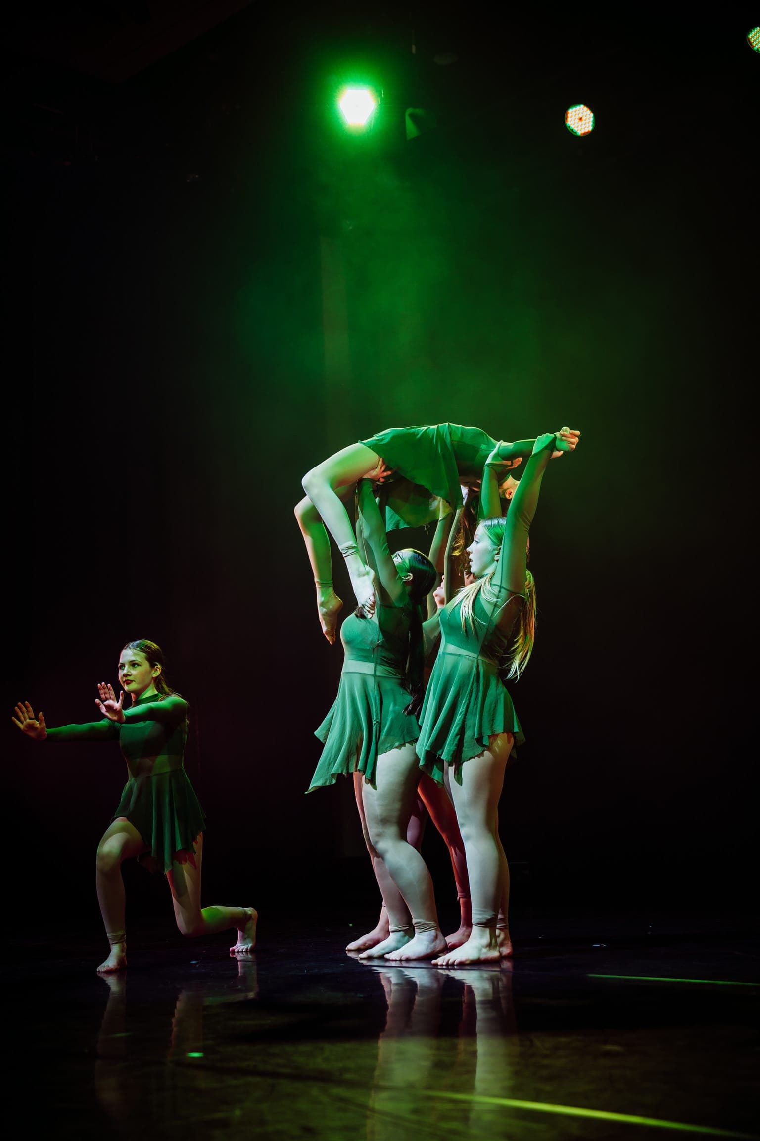 Contemporary dancers in a green-lit group lift