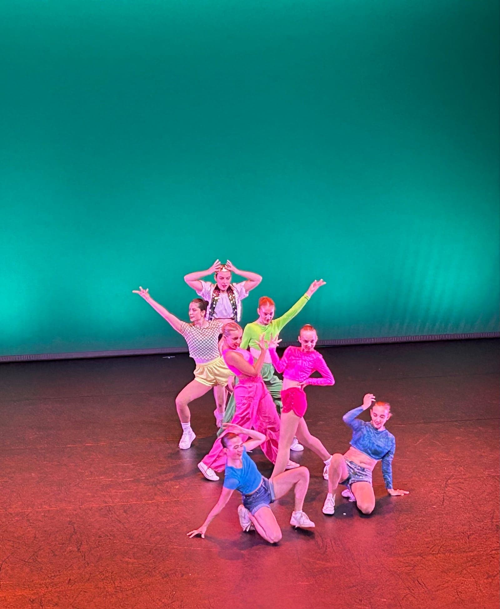 Jazz dancers in bright costumes against a teal backdrop