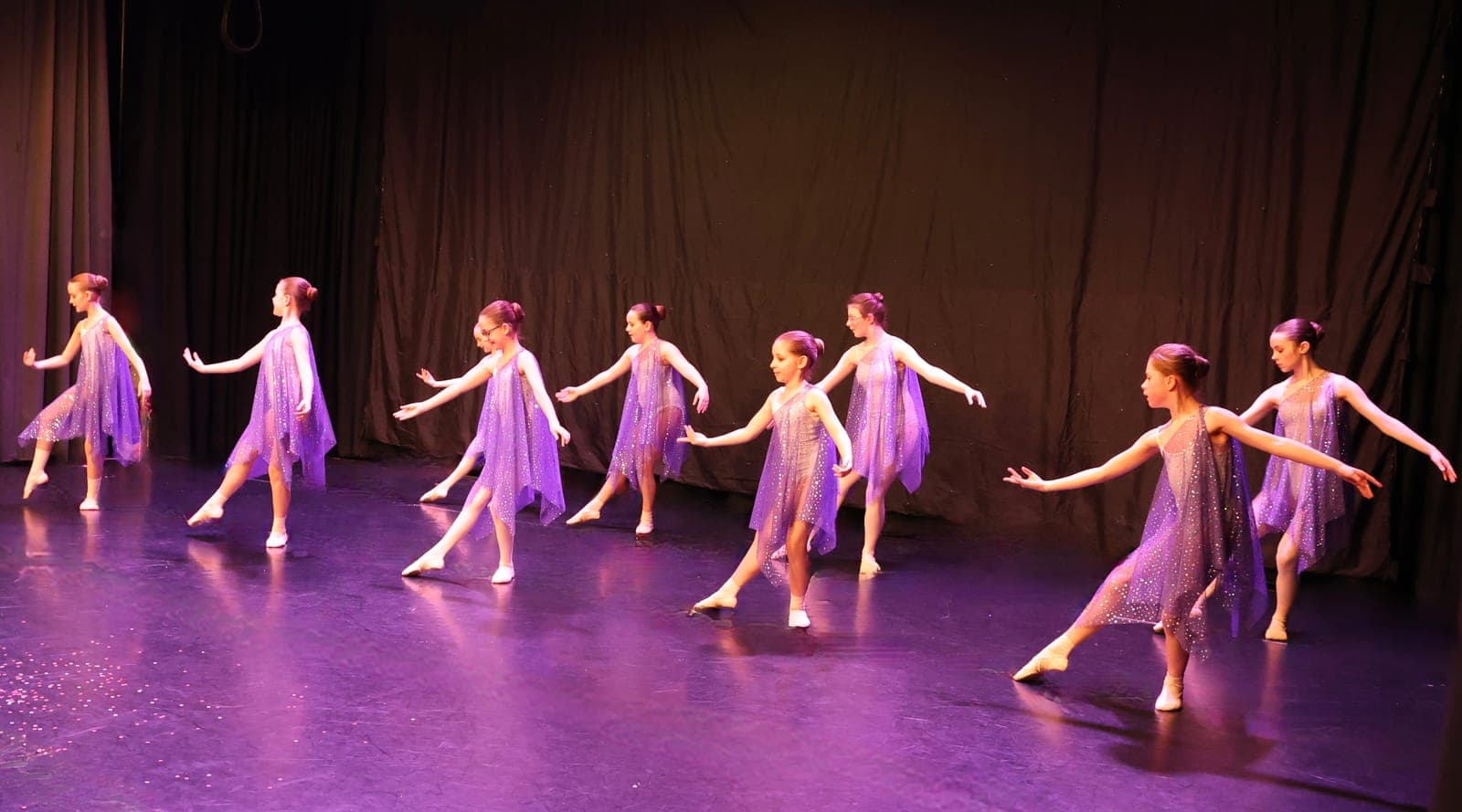 Young dancers in lilac dresses on a purple-lit stage