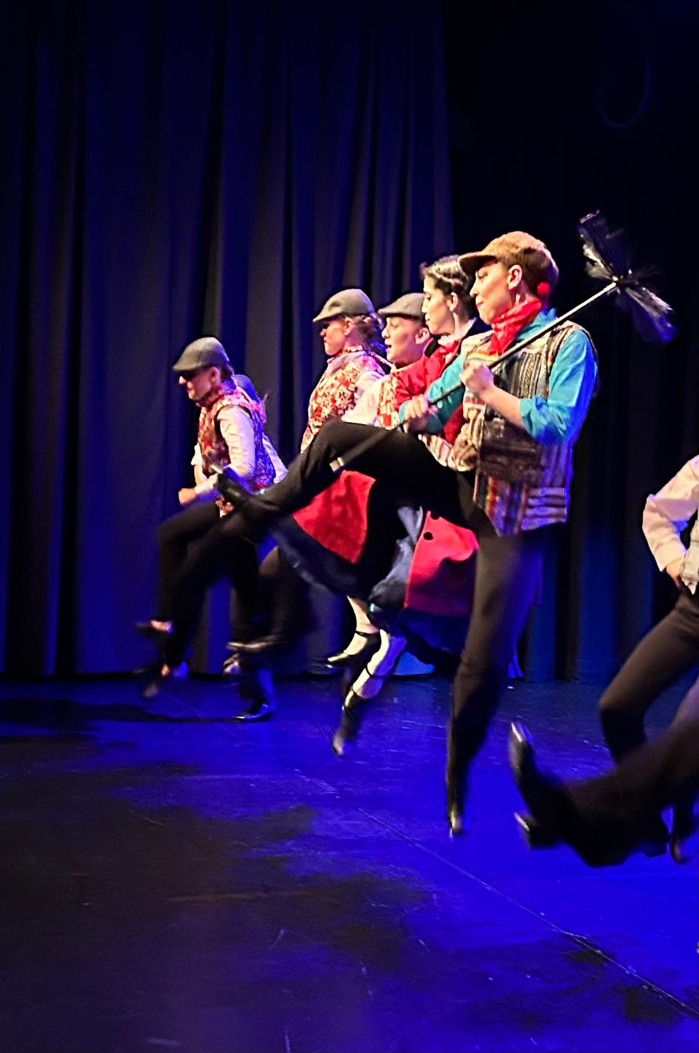 Musical theatre dancers in chimney sweep costumes kicking high on stage